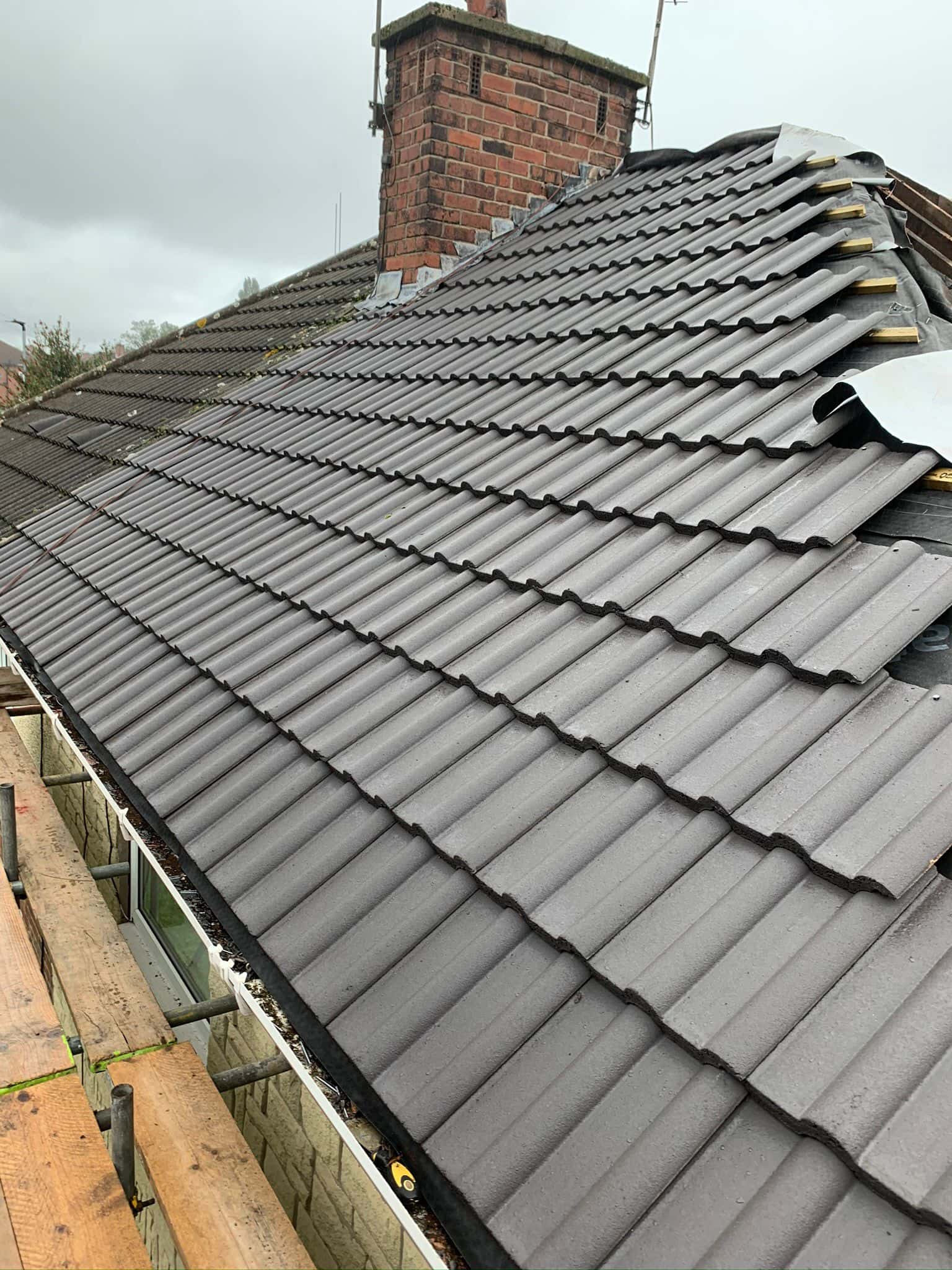 This is a photo of a hip roof which is being re-roofed. One side has new grey tiles already installed by Northampton Roofing Services